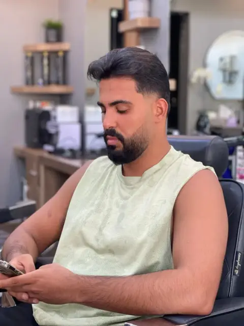 Low taper fade with textured brushed-back hair and a full boxed beard, styled at Barberhood in JVC, Dubai