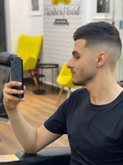Client checking his fresh high skin fade and cropped top in the mirror at Barberhood barbershop, JVC Dubai