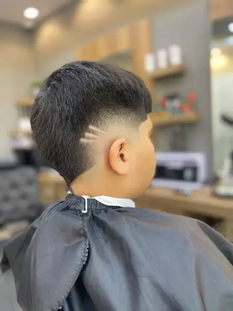 Junior burst-fade mullet with razored hair-design lines above the ear, cut at Barberhood, JVC Dubai