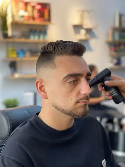 Barber detailing a classic pompadour with a high skin fade using a trimmer at Barberhood, JVC Dubai